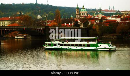 Besichtigungsboot Atlantida, das auf der Moldau in Prag, Tschechische Republik, mit der historischen Skyline der Stadt und der Nikolaikirche fährt Stockfoto