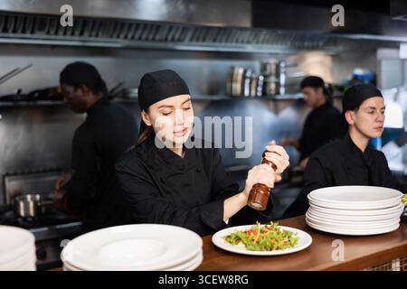 Weibliche Köche in schwarzem Uniform-Paprika-Salat in der Küche Stockfoto