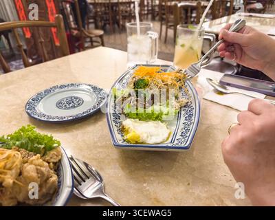 Person, die am asiatischen Restauranttisch mit einem Nudelgericht Eiergemüse auf traditionellem chinesischem Geschirr und geeistem Zitronentee Malacca malaysia speisen kann Stockfoto