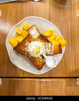 Blick aus der Vogelperspektive auf Honigtoast, serviert mit Eis und frischen Mangoblättern auf einem Holztisch. Malakka malaysia Stockfoto