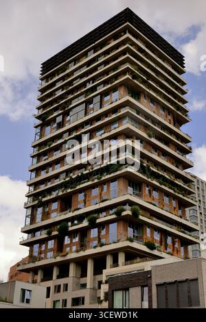 Mehrschichtiger Wohnturm mit bepflanzten Terrassen und Holzpaneelen über umliegenden Blöcken in Amsterdam, Niederlande, unter Wolken, von der Straße aus gesehen. Stockfoto