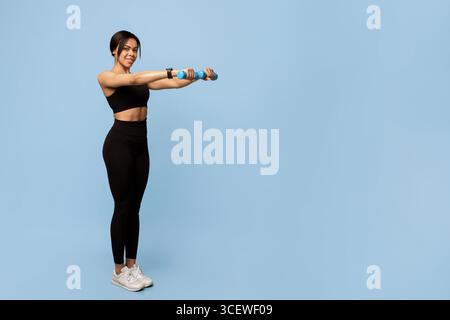 Armtraining. Glückliche junge afroamerikanische Sportlerin, die mit zwei Kurzhanteln auf blauem Hintergrund trainiert Stockfoto