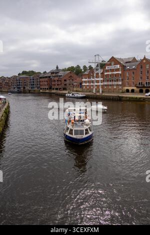 Passagierboot auf einem Stadtfluss mit Touristen an Bord, historische Backsteinhäuser im Hintergrund unter bewölktem Himmel Stockfoto