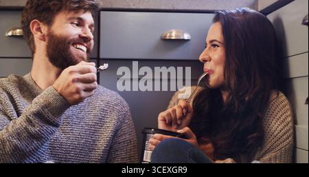 Happy, Paare und essen Eis auf dem Boden mit Liebe, teilen Dessert und verbinden sich miteinander. Lächeln Sie, Leute und entspannen Sie sich mit süßen Leckereien für romantische Gäste Stockfoto