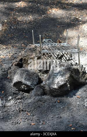 Lagerfeuer im Wald. Sicherheitssteine. Runder Kamin. Metallgrill in der Steinfeuerstelle auf dem Campingplatz im Freien bei sonnigem Wetter. Ätna, Sizilien. Stockfoto