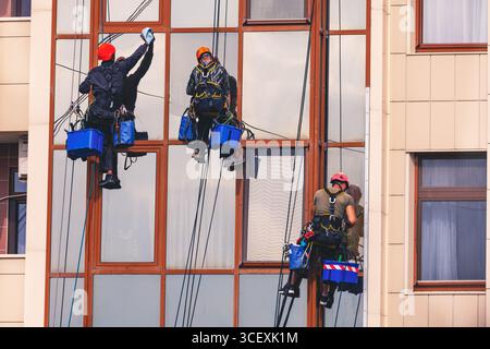 Professionelle Fensterreiniger an Seilen arbeiten effizient im Außenbereich moderner Gebäude, tragen Sicherheitsausrüstung und Helme. Teamwork und Präzision Stockfoto