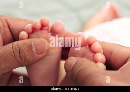 Nahaufnahme von erwachsenen Händen, die sanft ein Baby mit kleinen Füßen halten. Das Bild hebt den Größenkontrast zwischen den Händen und Füßen hervor und nimmt einen Moment von auf Stockfoto
