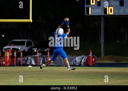 American Football Football-Spieler springt mitten in der Luft unter die Torpfosten, um beim Nachtspiel einen kritischen Fang zu erzielen – dynamische Action-Aufnahmen, die das sportliche Spiel in höchstem Maße einfangen Stockfoto