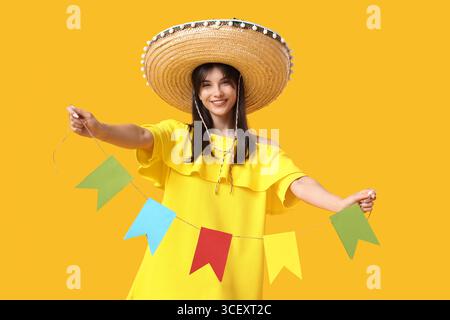 Junge Frau im Sombrero, die bunte Fahnen auf gelbem Hintergrund hält. Cinco de Mayo-Feier Stockfoto