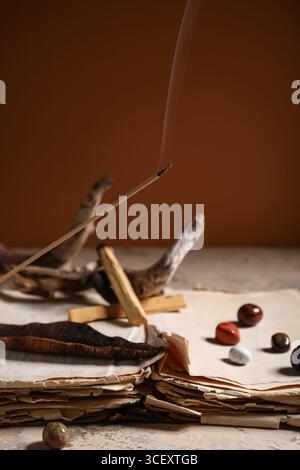 Komposition mit schwelendem Räucherstäbchen, Palo Santo, altem Buch und Steinen auf Leuchttisch Stockfoto