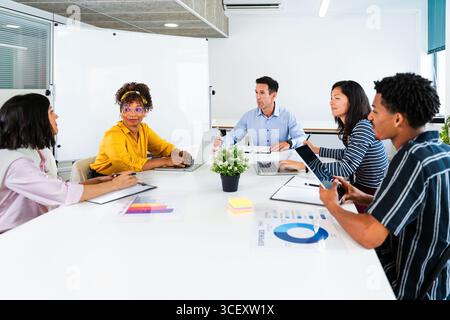 Verschiedene Geschäftsteams arbeiten während der Besprechung in modernen Büros an Projekten zusammen, analysieren Finanzdaten, verwenden Laptops und Tablets, teilen Ideen, und Stockfoto