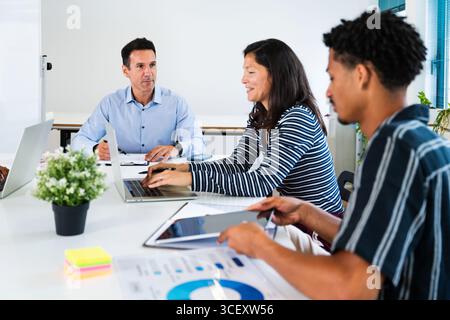 Geschäftskollegen arbeiten zusammen, analysieren Daten und verwenden Laptops und Tablets während eines produktiven Meetings in einem modernen Bürobereich Stockfoto