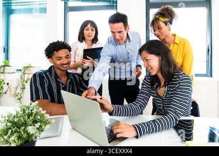 Ein vielseitiges Team von Fachleuten versammelte sich um einen Laptop und nahm an einer gemeinsamen Diskussion und Problemlösung in einem modernen Startup-Büro Teil Stockfoto
