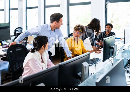 Büromitarbeiter diskutieren ein Projekt, arbeiten mit Desktop-Computern in einer hellen, modernen Büroumgebung zusammen, fördern die Teamarbeit und Stockfoto