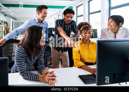 Ein vielseitiges Team von Fachleuten versammelte sich rund um Computer, arbeitete zusammen und zeigte auf den Bildschirm in modernen Büros, arbeitete in Startup-Projekten zusammen Stockfoto