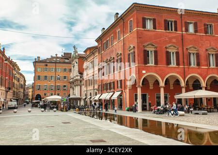 Modena, italien 20. august 2025: Die Menschen genießen die piazza roma in modena, italien, schlendern entlang des Wasserspiels und bewundern die farbenfrohen Gebäude Stockfoto