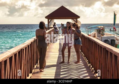 Dominicus, dominikanische republik 20. august 2025: Zwei Touristen machen Fotos von ihrem Freund, der auf einem Holzpier in dominicus, dominikanische republik posiert Stockfoto