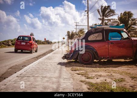 Isla mujeres, mexiko 20. august 2025: Ein roter volkswagen-Käfer parkt auf einem Bürgersteig in isla mujeres, mexiko, mit einem roten Taxi, das auf einem sonnigen Weg vorbeifährt Stockfoto