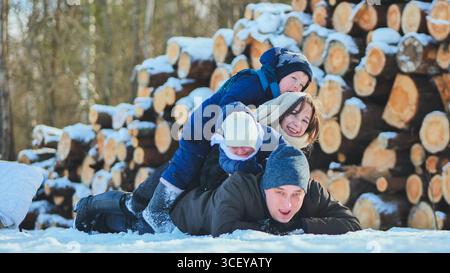 Familie spielt zusammen bei schneebedecktem Wetter und lacht in der Nähe von Holzhaufen während des Winters im Freien Stockfoto