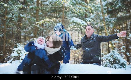Die Familie genießt einen fröhlichen Wintertag, spielt im Schnee inmitten der Bäume eines malerischen Waldes und schafft zusammen unvergessliche Erinnerungen Stockfoto