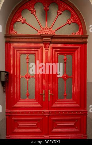 Verzierte rote Doppeltür aus Holz mit gewölbter Oberseite und dekorativen Glaspaneelen Stockfoto