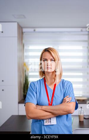 Ernsthafter Arzt mit überkreuzten Armen in der Klinik stehend in blauer Uniform Stockfoto