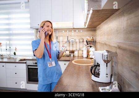 Die junge Ärztin genießt ihre Kaffeepause zu Hause und spricht am Telefon Stockfoto