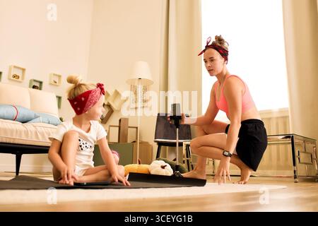 Eine Mutter und ihre Tochter verbringen an einem sonnigen Tag gemeinsam Yoga. Der gemütliche Wohnbereich verstärkt die warme und fröhliche Atmosphäre, h Stockfoto