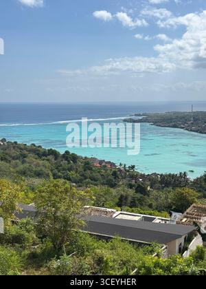 Panoramablick auf türkisfarbenes Wasser, üppige Hügel und Küstendorf in Nusa Penida, Bali, Indonesien, von oben unter einem klaren tropischen Sommerhimmel. Stockfoto