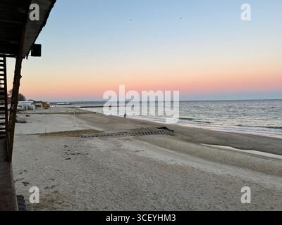 Ein sanfter rosafarbener Sonnenuntergang am Strand des Schwarzen Meeres, der sich vom rosa bis zum blauen Himmel erstreckt Stockfoto