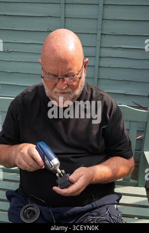 Mann, der die Elektronik mit einem Schraubendreher zusammenbaut. Senior-Mann, der im Ruhestand aktiv bleibt Stockfoto