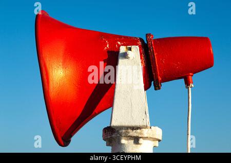 Ein rotes Schiffshorn ist auf einem Stahlgestell gegen einen blauen Himmel befestigt. Stockfoto
