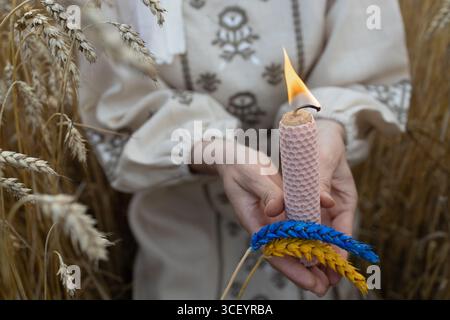 Brennende Kerze und zwei Weizenohren, gemalt in gelb-blauen Farben der ukrainischen Flagge, in den Händen der Frau auf Weizenfeld. Ein konzeptionelles Foto im Gedächtnis Stockfoto