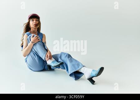 Stilvolle junge Frau sitzt anmutig auf dem Boden und strahlt Vertrauen in ihr modisches Outfit aus. Stockfoto