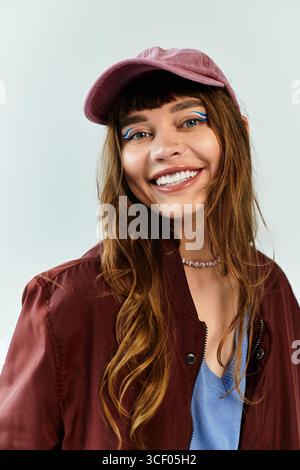 Eine selbstbewusste junge Frau in trendiger Kleidung lächelt breit und trägt einen einzigartigen Hut und ein auffälliges Make-up. Stockfoto