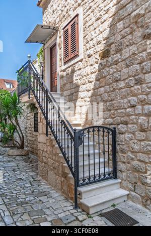 Wunderschöne Steintreppe mit einem kunstvollen schmiedeeisernen Geländer führt an einem sonnigen Sommertag zum Eingang eines alten europäischen Hauses Stockfoto