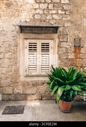 Der Charme eines historischen Dorfes: Ein altes Steingebäude mit geschlossenen Fensterläden und einer Topfpflanze, die eine friedliche und einladende Atmosphäre schafft. Traditiona Stockfoto