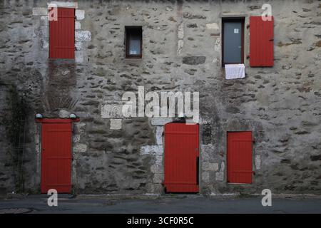 Alte graue Steinfassade mit roten Türen und Fensterläden Stockfoto