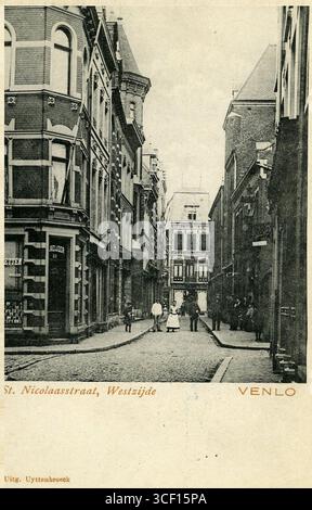 Eine Fotografie aus dem Jahr 1900, die St. Nicolaasstraat, später in Klaasstraat umbenannt, an der Kreuzung mit Nieuwstraat und Begijnengang zeigt. Das Foto zeigt die St. Nicolaaskerk (Klaoskerk) und ein lokales Bekleidungsgeschäft im Hintergrund. Stockfoto