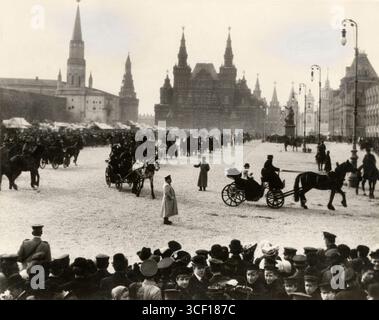Eine verschneite Szene auf dem Roten Platz in Moskau, wo eine Prozession von Pferdekutschen vorbeizieht. Im Hintergrund befinden sich der Kreml, das nationale historische Museum und Marktstände. Stockfoto
