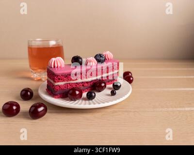 Ein Stück Kuchen mit rosa Zuckerguss und cremiger Füllung. Garniert mit frischen Heidelbeeren und Kirschen, serviert auf einem weißen Teller gegen einen rustikalen Stockfoto