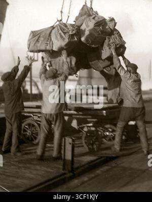 Während des Ersten Weltkriegs heben Arbeiter mit einem Kran Postsäcke aus dem Frachtraum eines Schiffes und legen sie auf einen Wagen für den Transport in Hoek van Holland, 1916. Stockfoto