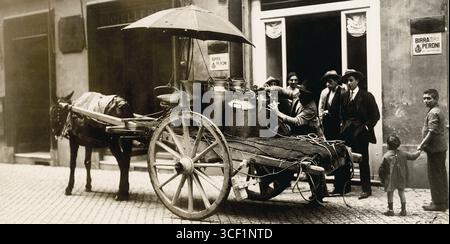 1925 stand ein Milchhändler neben einem Pferdewagen mit Milchkannen vor einem Geschäft, in dem sich Menschen in Italien versammelten. Stockfoto