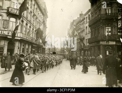In den Straßen von Lüttich werden deutsche Truppen zurückgezogen, begleitet von lokalen Zivilisten. Flaggen hängen an Gebäuden, wenn die Soldaten die Stadt verlassen. Lüttich, Belgien, 1918. Stockfoto