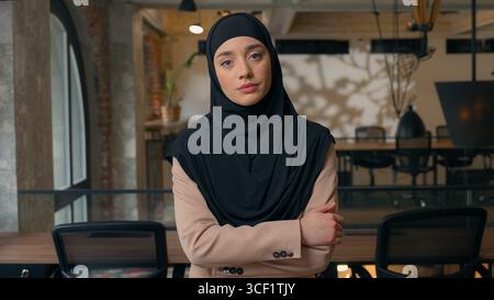Islamisch-indische Geschäftsfrau im Büro, die mit überkreuzten Händen posiert. Muslimische Mädchen Praktikantin Geschäftsfrau in Hijab weibliche ceo steht bei Stockfoto