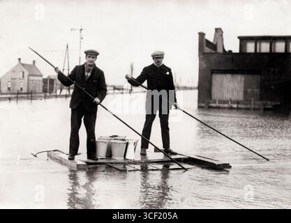 Im Jahr 1926 werden in Cuyk, Niederlande, lebenswichtige Lebensmittel per Boot an Häuser geliefert, in denen die Bewohner noch nicht evakuiert sind. Zwei Männer stehen neben Eimern und Kisten und führen das Boot. Cuyk, Niederlande, 1926. Stockfoto