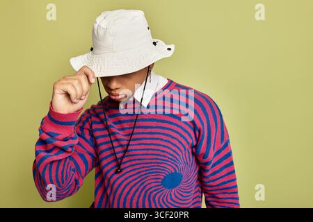 Ein stylischer junger Schwarzer posiert in einem abstrakten, gestreiften Sweatshirt vor einem hellgrünen Hintergrund. Stockfoto