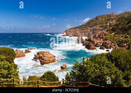 Türkisfarbene Wellen gegen zerklüftete Klippen und Felsformationen in Costa Paradiso, Sardinien, umgeben von üppiger mediterraner Vegetation. Stockfoto