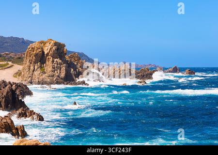 Mächtige Wellen krachen an der zerklüfteten Küste von Costa Paradiso, Sardinien, unter einem leuchtend blauen Sommerhimmel gegen hoch aufragende Felsformationen. Stockfoto