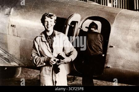 Amelia Earhart (1897–1937), eine Pionierin der amerikanischen Fliegerei, wird in ihrem Fluganzug neben ihrer Lockheed Electra auf dem Parnamerim Airfield in Brasilien gezeigt, mit Fred Noonan im Hintergrund. Das Foto ist vom Juni 1937. Stockfoto